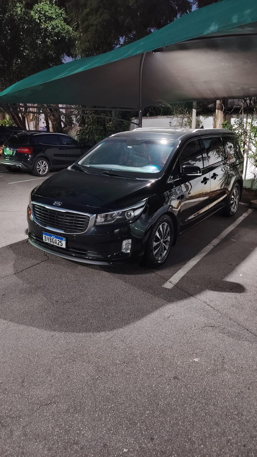 Minivan Kia Carnival preta estacionada sob toldo