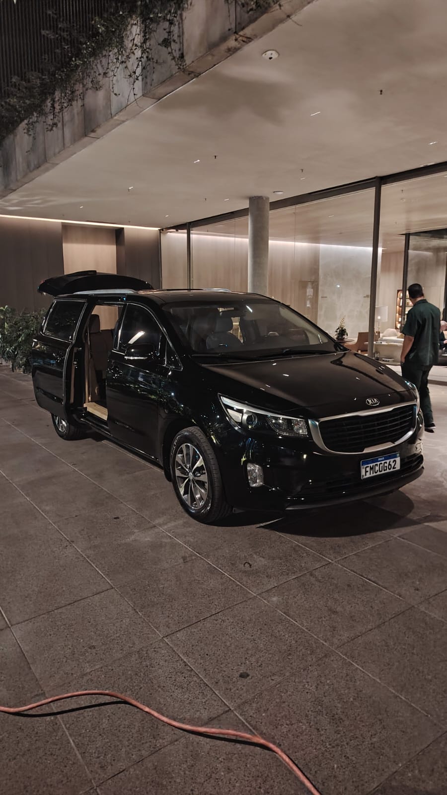 Minivan Kia Carnival preta na entrada de hotel à noite, com porta lateral aberta